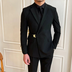 A man wears a slim-fit black suit jacket featuring a gold buckle closure and matching trousers.