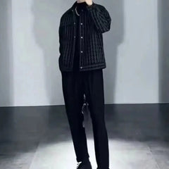 A man wears a black and grey houndstooth patterned jacket with a square collar over a black shirt.