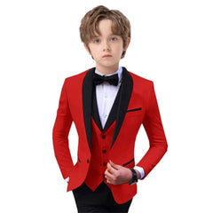 A boy wears a red three-piece suit featuring a black shawl lapel blazer, vest, and bow tie.