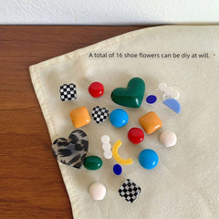 A collection of sixteen colorful, patterned, and shaped shoe charms arranged on a fabric surface.