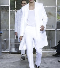 A man wears a white two-piece suit featuring a long jacket and matching trousers.