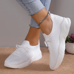 A pair of white mesh lace-up sneakers with a platform sole worn by a person.