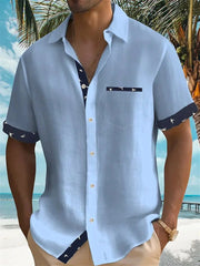 A light blue short-sleeved men's shirt with dark patterned trim on the cuffs, placket, and pocket.