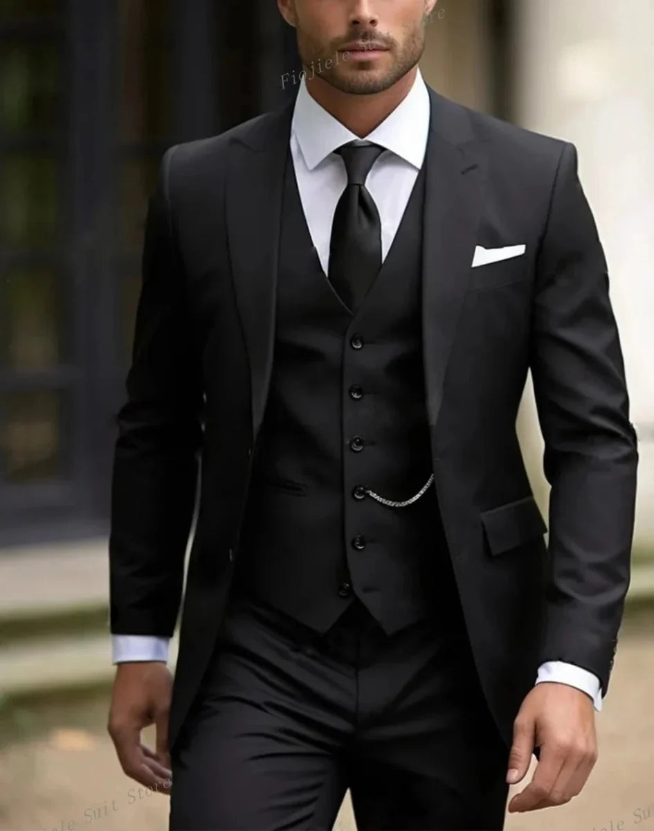 A man wearing a black three-piece suit with a white shirt, black tie, and pocket chain.