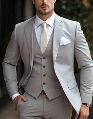 A man wearing a light grey three-piece suit with a white shirt, cream tie, and pocket square.