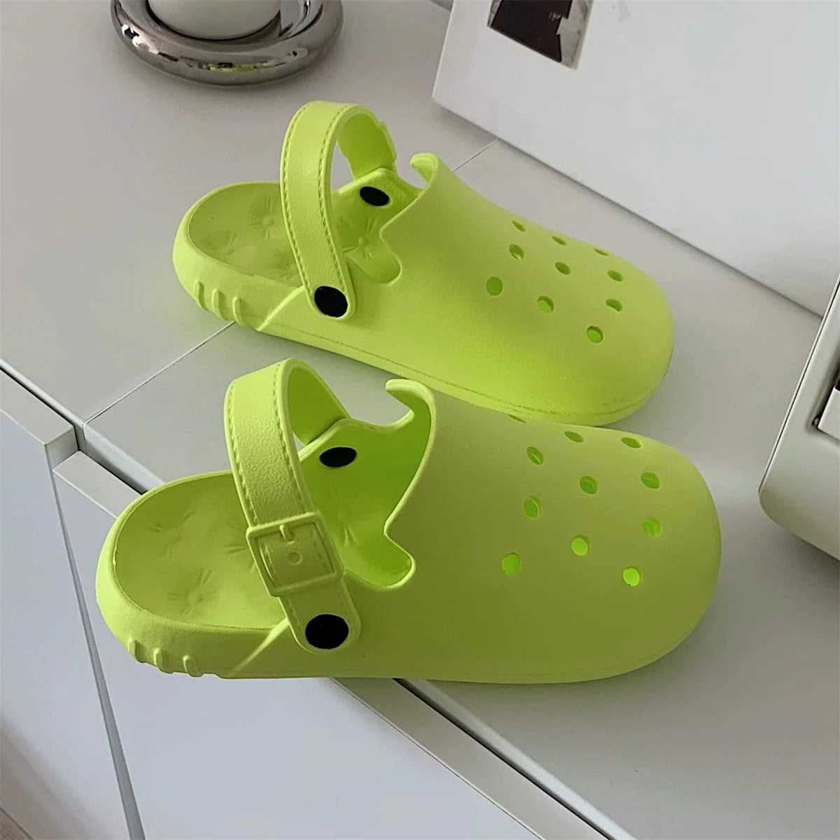 A pair of lime green EVA hole shoes with adjustable buckled heel straps on a white surface.