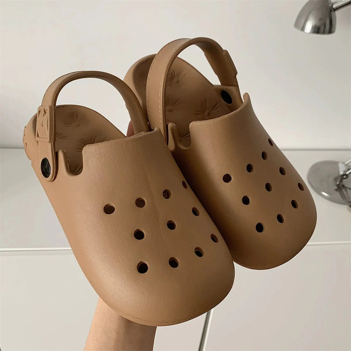 A pair of tan EVA foam clogs with a perforated upper and an adjustable heel strap.