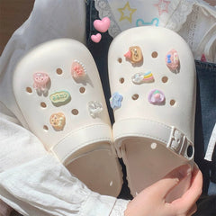 A pair of cream-colored EVA hole shoes decorated with various colorful cartoon charms.