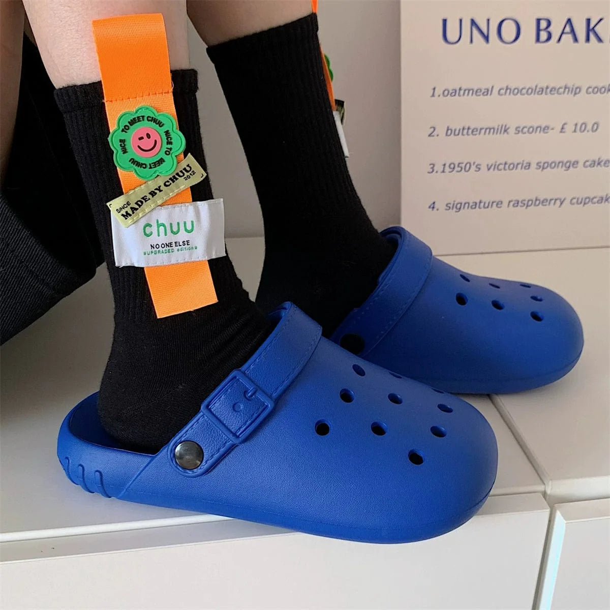 A pair of bright blue EVA hole shoes worn with black socks featuring orange decorative straps.