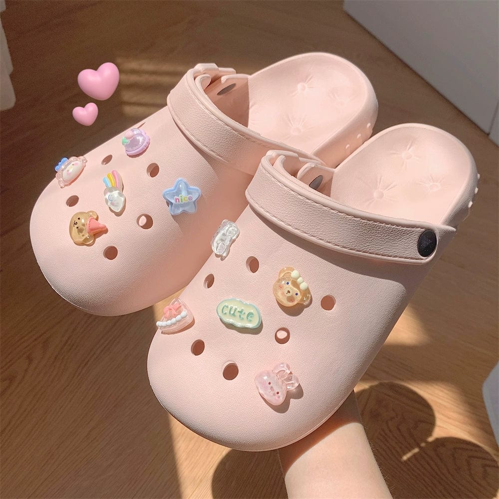 A pair of light pink EVA clogs decorated with various colorful cartoon charms.