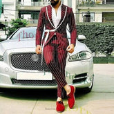 A man wears a burgundy striped two-piece suit with a white shirt and red shoes by a car.