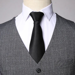 Un hombre viste un chaleco gris texturizado sobre una camisa blanca con una corbata negra.
