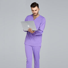 A man wearing a light purple unisex jogger-style medical scrub set with a laptop.