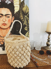 A beige woven straw bucket bag with a single braided handle and a zippered interior.