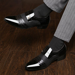 A pair of black pointed-toe slip-on dress shoes with a textured panel and metallic accent.