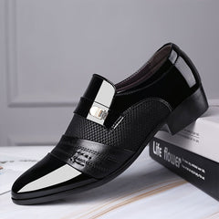 A black pointed-toe slip-on dress shoe with a textured panel and a metallic decorative buckle.