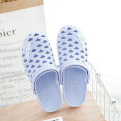 A pair of light blue rubber slip-on clogs with a hollow geometric pattern and flat soles.