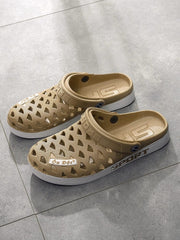 A pair of tan rubber clogs with a hollow-out design and white soles on a grey tiled floor.