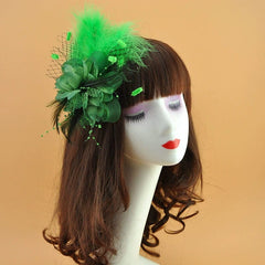A green floral hair clip featuring feathers, netting, and beaded accents on a mannequin head.