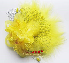 A bright yellow floral hair clip featuring layered fabric petals, delicate netting, and soft feathers.