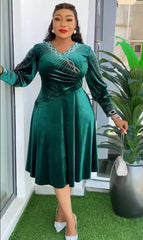 A woman wears a knee-length emerald green velvet dress with long sleeves and rhinestone detailing.