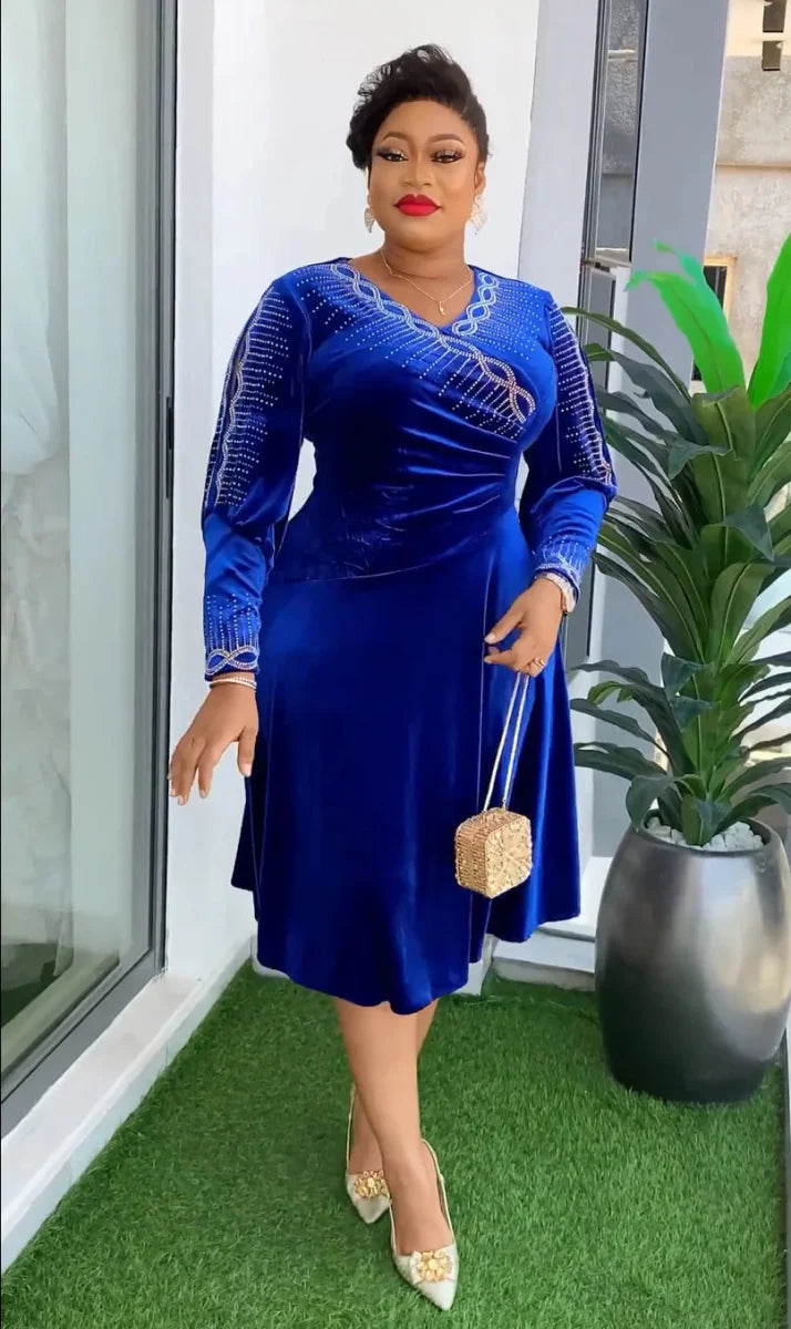A woman wears a royal blue velvet knee-length dress with long sleeves and silver beaded accents.