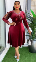 A woman wears a long-sleeved, knee-length burgundy velvet dress with rhinestone embellishments.