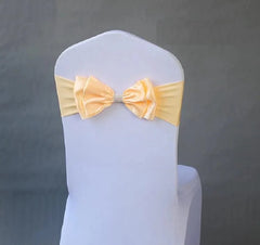 A pale yellow satin bow sash with a rhinestone center fitted on a white chair cover.