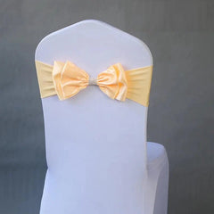 A pale yellow satin bow chair sash with a rhinestone center band fitted on a white chair cover.