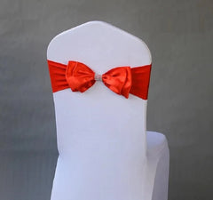 A white chair cover decorated with a pre-tied red satin bow featuring a rhinestone center band.