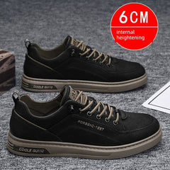 A pair of black casual men's sneakers with tan laces and soles on a grey surface.