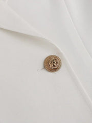 A close-up of a white blazer dress featuring a gold lion-embossed button.