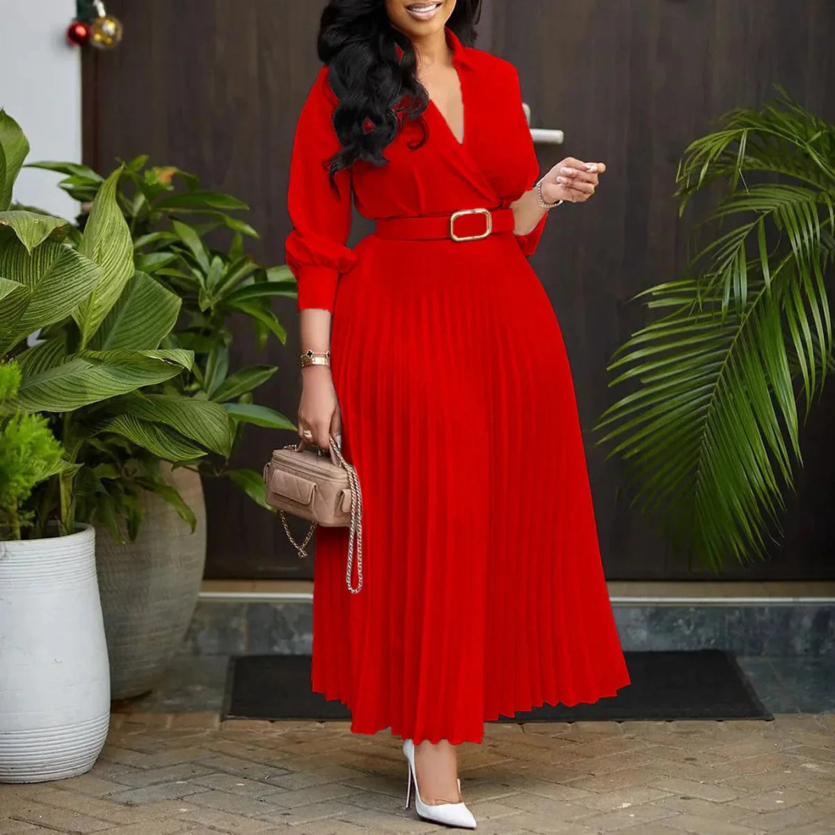 A woman wears a long-sleeved red V-neck pleated dress with a matching belt and white heels.