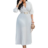 A woman wears a white long-sleeved V-neck pleated midi dress with a matching belt.