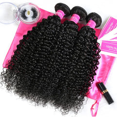 Three bundles of curly black human hair extensions displayed on a pink satin bag with eyelashes.