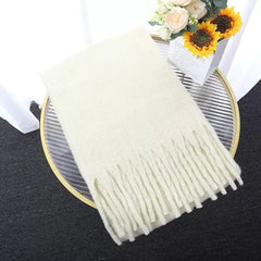 A soft, solid-colored cream winter scarf with long tassels, displayed on a glass table.