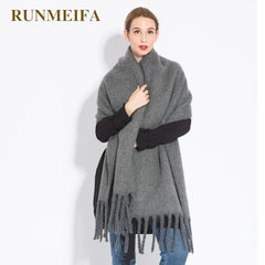 A woman wears a thick, grey, solid-colored cashmere-blend scarf with fringe detailing.