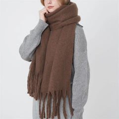 A woman wears a thick, solid brown cashmere-blend scarf with long tassels.