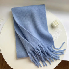 A soft, solid light blue cashmere-blend scarf with fringe ends, displayed on a white surface.