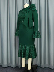 A dark green midi dress with a high neck, bow detail, long sleeves, and sequin patchwork.