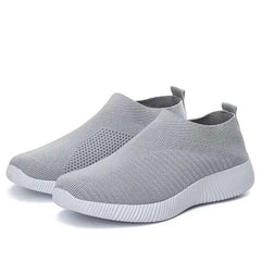A pair of light gray slip-on sneakers with a textured knit upper and a white ridged rubber sole.