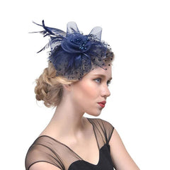 A woman wears a navy blue mesh fascinator hat adorned with a fabric flower, feathers, and beads.