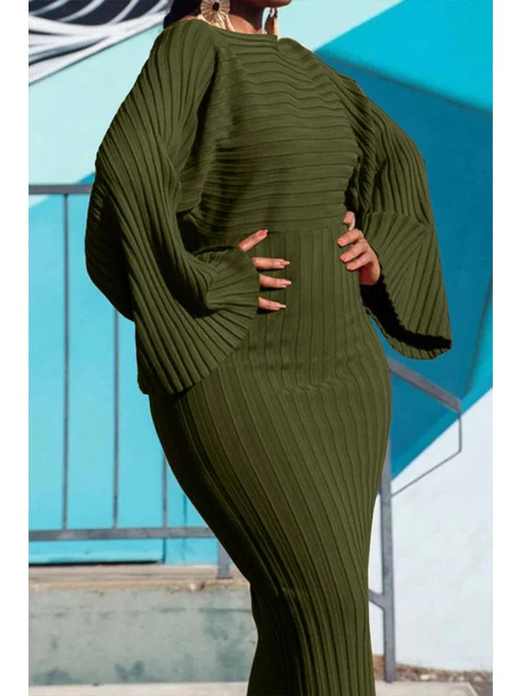 A woman wears an olive green, ribbed knit midi dress with batwing sleeves and a round neckline.