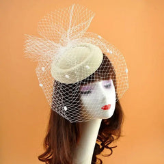 A beige felt fascinator hat with a white fishnet veil and small plush polka dot accents.