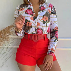 A woman wears a long-sleeved floral print shirt tucked into bright red shorts with a belt.