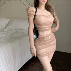 A woman wears a beige two-piece set featuring a long-sleeved ruched top and a matching mini skirt.