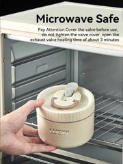 A hand places a beige, round, stainless steel lunch box with a valve lid into a microwave.