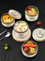 Three round, off-white and khaki insulated bento lunch boxes filled with various foods are arranged on a dark surface with a spoon and chopsticks.