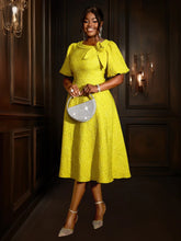 A woman wears a yellow jacquard midi dress with puff sleeves and a 3D flower detail.