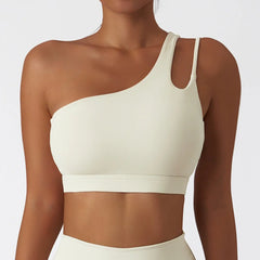 A cream-colored, one-shoulder sports bra with a cutout detail on the left strap.